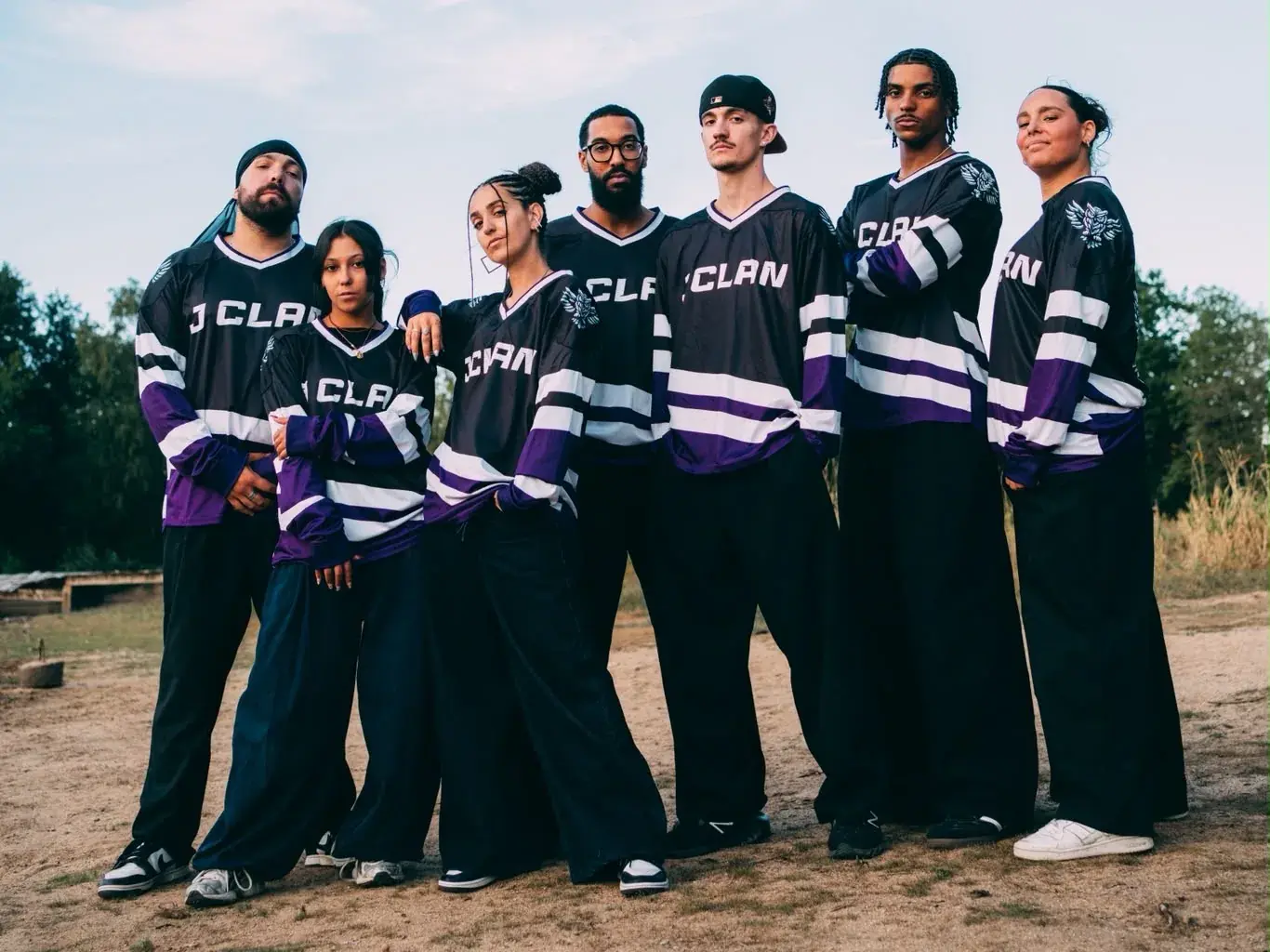 The seven J Clan performers wearing company jerseys, gathered outdoors at sunset.